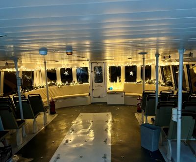 Empty ferry cabin at dusk with rows of seats and reflective windows.